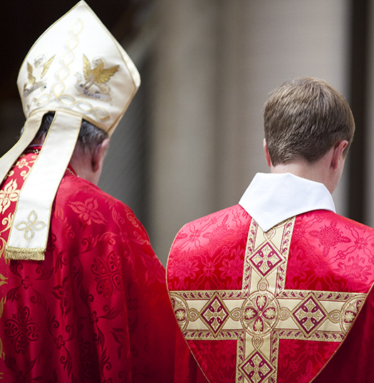 Episcopal bishop and assistant in red liturgical garments