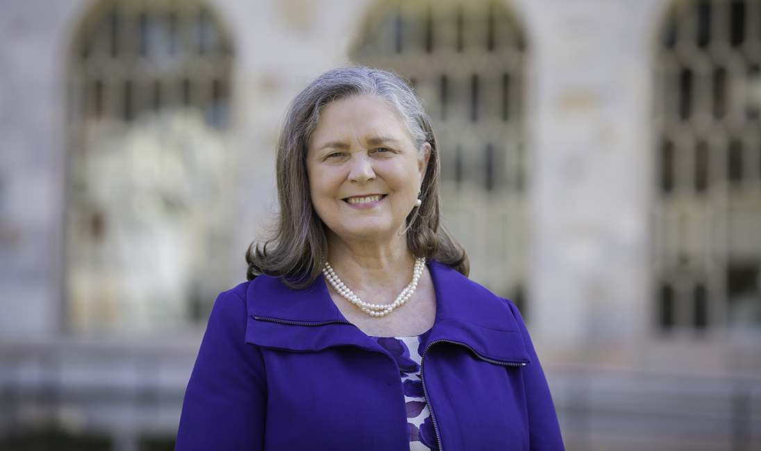 Jan Love in blue jacket standing in front of arched windows