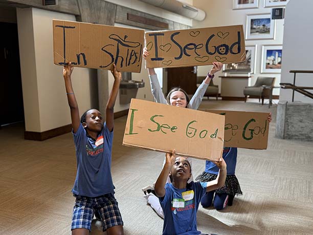Children holding handmade cardboard signs saying I see God and In ships.