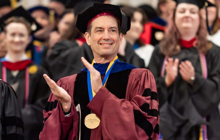 Jonathan Strom in academic regalia, applauding in front of group of graduates